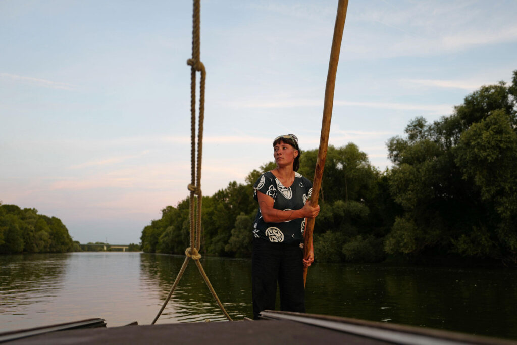 Une jeune femme dirige un bateau de Loire avec une bourde, au soleil couchant.