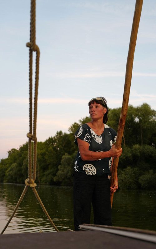 Une jeune femme dirige un bateau de Loire avec une bourde, au soleil couchant.