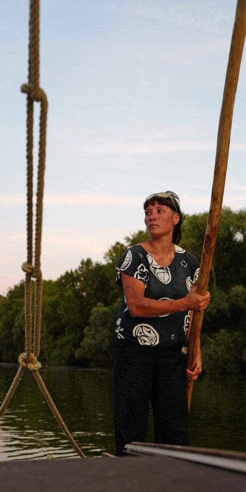 l1250843 Une jeune femme dirige un bateau de Loire avec une bourde, au soleil couchant.